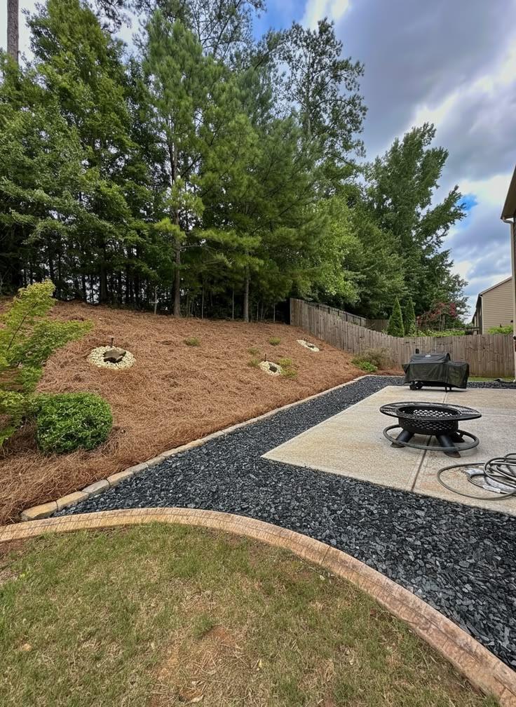 Backyard outdoor living area with a fire pit, seating, and gravel driveway leading toward a landscaped home in Kernersville, NC.